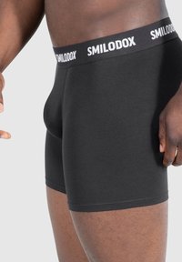 Boxer shorts in cotone nero con una texture liscia, dotati di una cintura con logo bianco. Il design è aderente e si estende fino a metà coscia.
