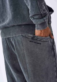 Sudadera de tela cepillada en gris, con puños y cintura acanalados, acompañada de pantalones joggers a juego que cuentan con un bolsillo lateral y un detalle de logo.