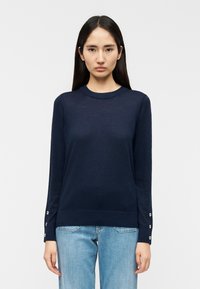 Μπλε ναυτικό πουλόβερ με μακριά μανίκια και στρογγυλή λαιμόκοψη, με ασημένιες πόρπες στα μανίκια και απαλή, λεία υφή.