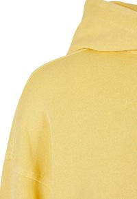Felpa gialla con un tessuto a coste e testurizzato. Presenta una vestibilità comoda e un cappuccio grande, evidenziando elementi di design casual e morbidi.