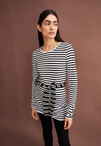 Lange mouwen, gestreepte top in zwart en wit, voorzien van een geknoopte, contrasterende zwart-witte riem. Gladde stof en ronde halslijn.