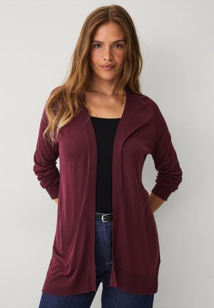 Bordeaux lichte cardigan met lange mouwen, open voorkant en geribbelde manchetten. Gecombineerd met een zwarte top en blauwe jeans. Zachte textuur.
