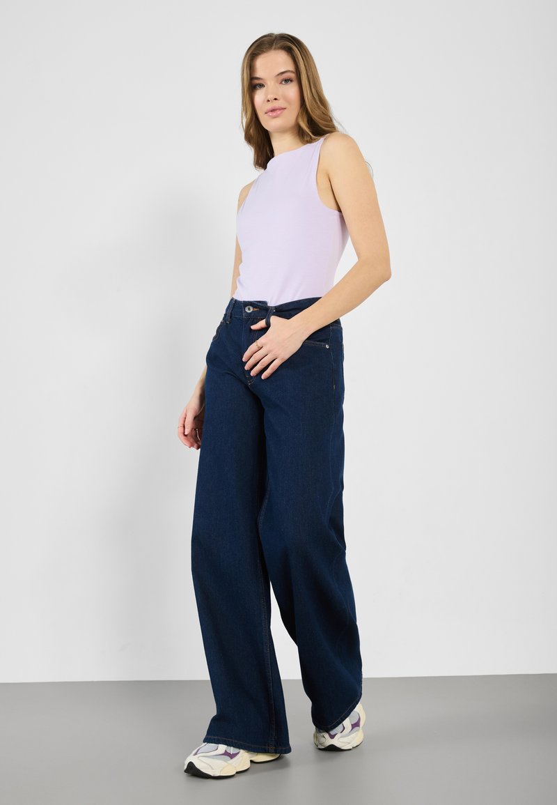 Lys lilla ermel�øs topp kombinert med vide mørkeblå denimjeans. Har en jevn tekstur og en klassisk knappestolpe.