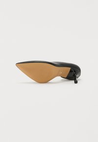 Black high-heeled shoe with a pointed toe, glossy surface, and a tan rubber sole featuring horizontal ribbing for traction.