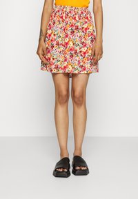 Jupe à imprimé floral avec une ceinture froncée, présentant des couleurs vives comprenant le rose, l'orange et le vert. Associée à des sandales noires à enfiler.