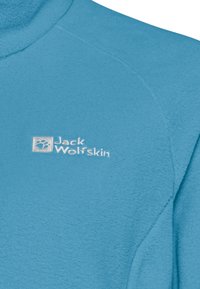 Maglione in pile blu chiaro con colletto alto e logo "Jack Wolfskin" bianco. La texture è morbida con cuciture visibili sui lati.
