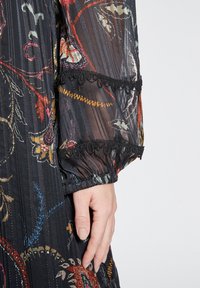 Musta läpinäkyvä kangas, jossa on värikkäitä kukkakirjontoja ja poimutuksia. Käänteet hihassa, jossa on koristeellinen musta pitsireunus ja elastista keräilyä.