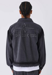 Giacca in denim nera con bordi sfrangiati, dettagli usurati e una vestibilità ampia. Caratterizzata da un design posteriore con motivi cuciti e chiusura con bottoni.