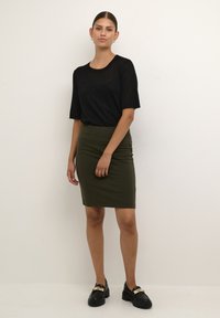 Top scurt negru cu finisaj texturat, asortat cu o fustă opacă de culoare verde măslin și pantofi loafers negri, cu toc masiv, având accente din aur.