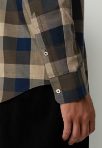 Cotton plaid shirt in beige, blue, and brown. Features buttoned cuffs and a curved hem. Light texture, modern fit.