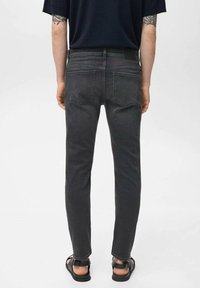 Jeans de mezclilla gris oscuro con corte ajustado, con un reverso liso que tiene dos bolsillos y un sutil detalle de costura. Llevados con sandalias negras.