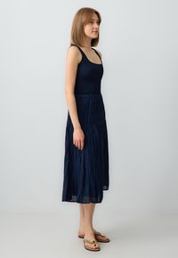 Top a righe di colore blu navy abbinato a una gonna fluida e plissettata. La gonna è di lunghezza media con un design testurizzato e una vita elasticizzata.