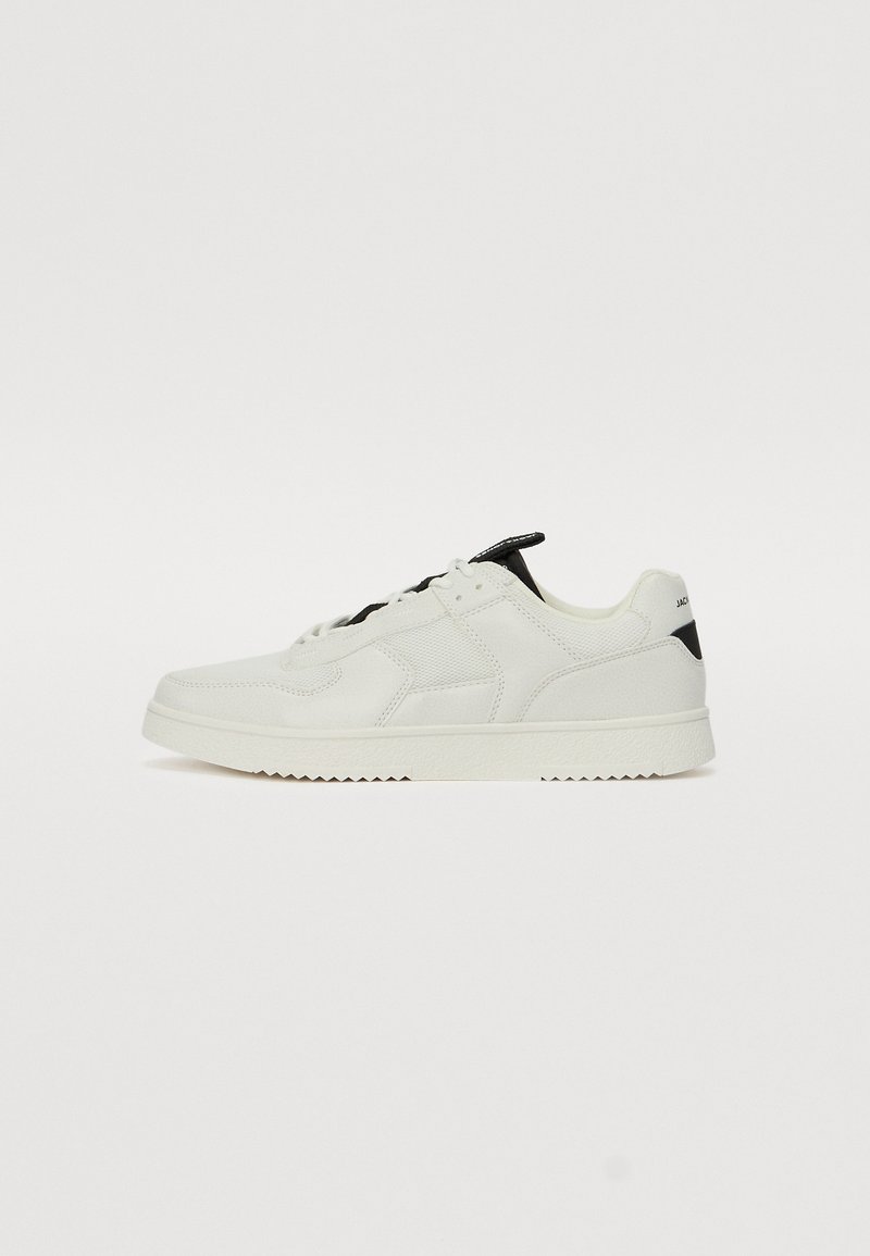 White sneaker featuring a mix of smooth and textured material, black accents on the heel, round toe design, and a stitched pattern.