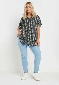 Camicia a maniche corte bianca e nera a fantasia, abbinata a jeans skinny azzurri e sneakers bianche.