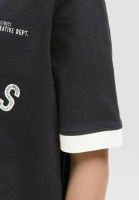 Camiseta negra de manga corta con puños blancos y texto impreso "DEPARTAMENTO CREATIVO DEL DISTRITO." en blanco contrastante en el frente.