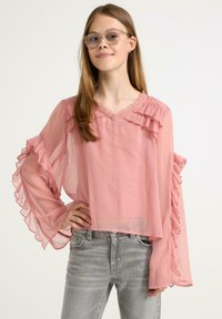 Rosa rüschenshirt mit langen, luftigen Ärmeln und V-Ausschnitt; leichtes und durchsichtiges Material mit strukturiertem Finish, kombiniert mit grauen Jeans.
