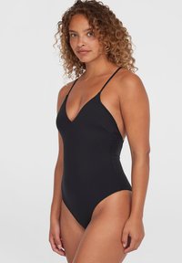 Maillot de bain une pièce noir avec un décolleté plongeant, des bretelles fines et une coupe mi-haute au niveau des jambes. Tissu lisse avec une finition mate. Design simple et ajusté.