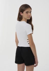 Top bianco a maniche corte con dettagli a taglio sui lati, abbinato a pantaloni corti neri. Presenta un design aderente e un tessuto morbido e strutturato.