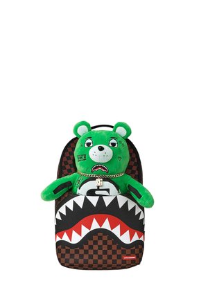 Oso de peluche verde con tatuajes faciales y cadena de oro dentro de una mochila marrón a cuadros con un diseño de boca de tiburón roja y blanca.