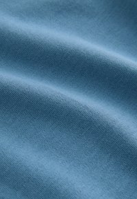 Tissu doux bleu clair avec une texture fine et uniforme de maille et des plis doux créant des ombres et des reflets subtils.
