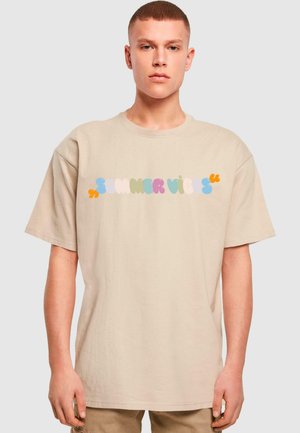 Beige oversized t-shirt lavet af bomuld, med farverige "SUMMER VIBES"-tekster i forskellige bobletegn henover brystet. Korte ærmer.