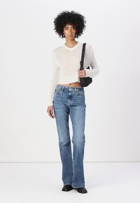 White, cropped sweater with a lightweight, textured appearance paired with blue flared jeans. Model holds a small, black handbag.