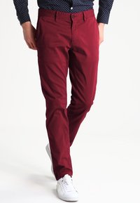 Burgundy chinos gjorda av bomull, med rak skärning, framfickor och bälteshällor, kombinerat med vita sneakers.