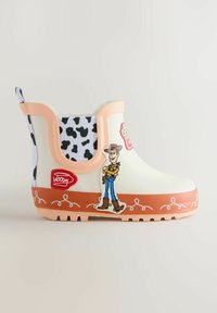 Gyermek fehér és tejbarna esőcsizma fekete tehénmintás díszítéssel, Woody figurával és a Toy Story logóval az oldalán.