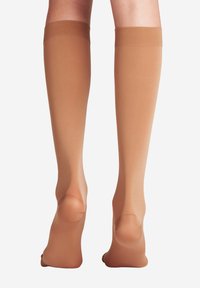 Calze beige fino al ginocchio con una texture liscia e lucida. Presentano un colore uniforme, punta rinforzata e un elastico nella parte superiore per supporto.