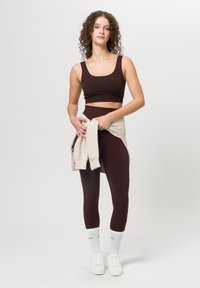 Brązowy crop top i pasujące legginsy z wysokim stanem, zestawione z jasnobeżowym swetrem związanym w talii oraz białymi trampkami.