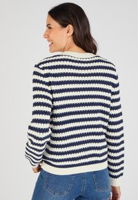 Marineblauw en crèmekleurig gestreept trui met een gestructureerd breipatroon, ronde hals en geribbelde boorden en onderkant. Gekocht met blauwe spijkerbroek.