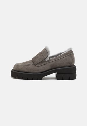 Mocassins en daim gris avec un bout arrondi, une doublure en fourrure et une semelle extérieure en caoutchouc noir épaisse avec un motif en zigzag. Détail décoratif de sangle sur le dessus.
