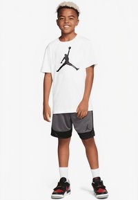 Hvid kortærmet t-shirt med sort Jordan-logo, kombineret med sorte mesh-shorts med sort kant forneden og Jordan-logo. Sorte og røde sneakers.