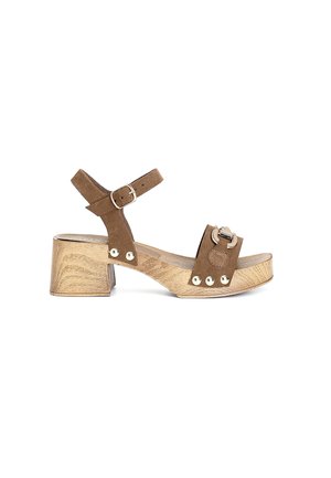 Sandali con tacco in suede marrone, dotati di una fascia ampia e di una fibbia. Il tacco a blocco con texture legno e i chiodini metallici mettono in risalto i dettagli del design.