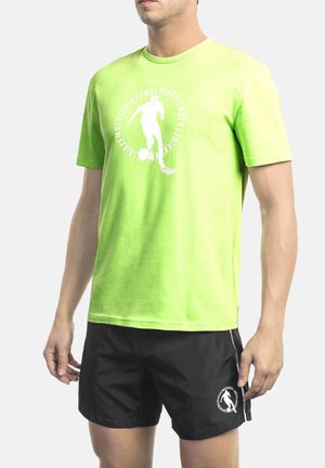 Bright green cotton T-shirt with a circular white graphic and text, worn with black shorts featuring a similar graphic on the leg.