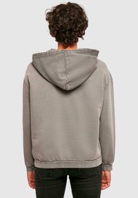 Grå hoodie med dragsko i huvan, ribbade ärmslut och nederkant, slät textur och en avslappnad passform, sedd bakifrån.