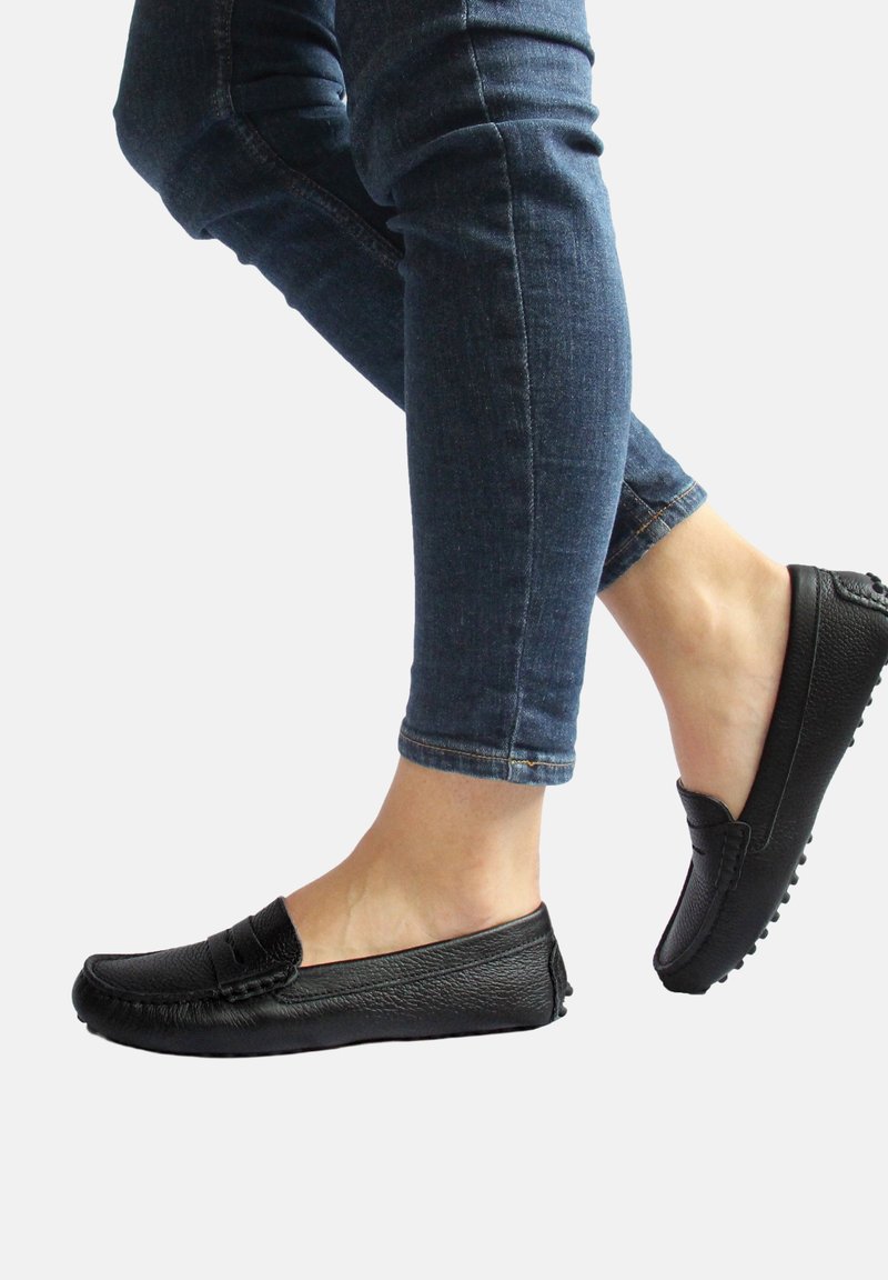 Schwarze Lederloafers mit strukturiertem Finish, im Slip-On-Design und mit Gummisohle. Kombiniert mit hochgekrempelten Jeans, die einen lässigen Schnitt zeigen.