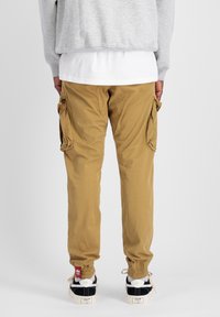 Khaki cargo kalhoty s bočními kapsami, šňůrkovými kotníky a standardním střihem. Nosené s bílými a černými teniskami.