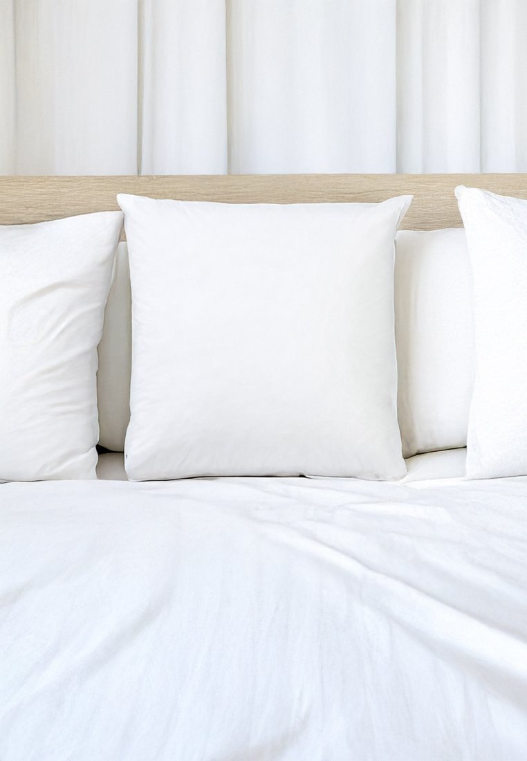 Biała poduszka w kształcie kwadratu na łóżku z białym prześcieradłem i dodatkowymi białymi poduszkami, charakteryzująca się gładką teksturą i minimalistycznym wzornictwem.