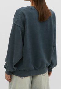 Donkerblauwe oversized sweatshirt met verlaagde schouders, ribgebreide manchetten en onderrand. De stof lijkt zacht met een licht versleten textuur.