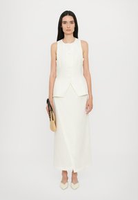 White linen sleeveless top with a fitted bodice, button detailing, and a high-low hem, paired with a matching wrap skirt.