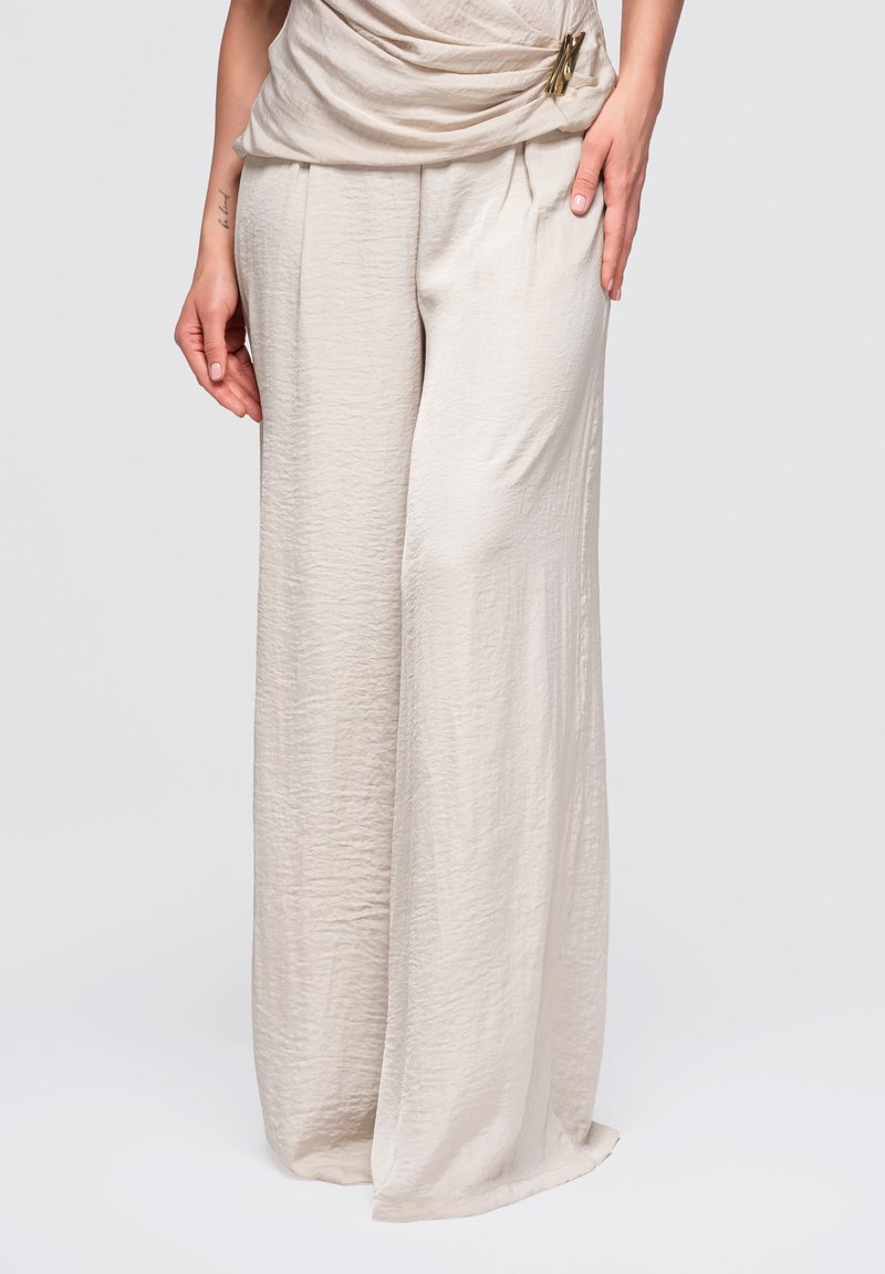 Pantalon large beige clair texturé avec une coupe ample, associé à un haut drapé assorti et un petit détail d'épingle à la taille.