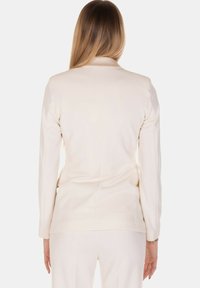 Blazer color crema con maniche lunghe, taglio sartoriale e texture liscia. Presenta una spacco singolo sul retro per facilitare il movimento.