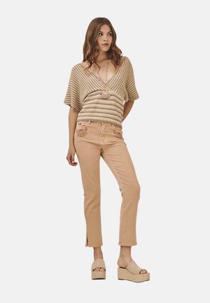 Top de punto beige con mangas amplias, combinado con pantalones vaqueros beige claros con bolsillos bordados. La modelo lleva sandalias de plataforma ligeras.