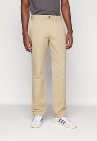 Khaki chino's met een rechte pasvorm, voorzien van een knoopsluiting, riemlussen en zijzakken, gecombineerd met witte sneakers.