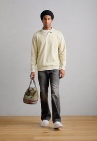 Világos sárga pulóver, sötétszürke farmernadrág, fehér tornacipő, olívazöld sporttáska sötétbarna díszítésekkel. Egyszerű háttér, fapadló.