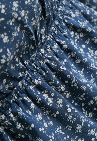 Tessuto blu navy con motivo floreale bianco, caratterizzato da una texture arricciata e cuciture elastiche per un aspetto aderente. Materiale in cotone morbido.