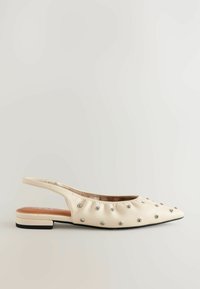 Beige slingback-lat puolikorkealla kantapäällä, valmistettu nahasta, jossa on kerrostettu rakenne ja hopeiset niittikoristeet. Teräväkärkinen muotoilu ja matala lohkarekorko parantavat designia.