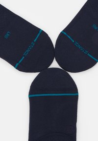 Navy ankle socks made of soft fabric, featuring light blue accent stripes and textured detailing on the heel with branding on the side.