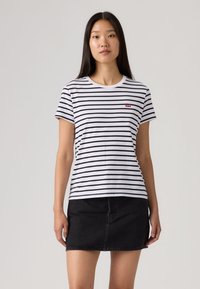 Λευκό T-shirt με μαύρες οριζόντιες ρίγες, στρογγυλή λαιμόκοψη και κοντά μανίκια. Διαθέτει μικρό κόκκινο λογότυπο στο αριστερό στήθος. Συνδυασμένο με μαύρη τζιν φούστα.